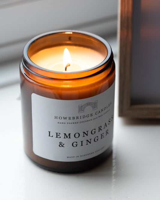 Candle in an amber jar labeled 'Lemongrass & Ginger' by Howebridge Candles on a white surface.