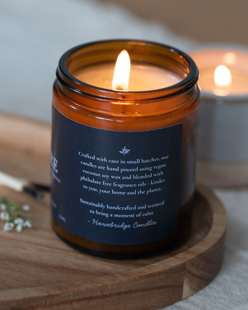Candle in an amber glass jar with a wooden coaster on a light background. Black label with detail on the side. Scent incense, sandalwood and frangipani. A rich Incense and slightly floral, the perfect candle to find inner balance, meditate or light during a yoga session.