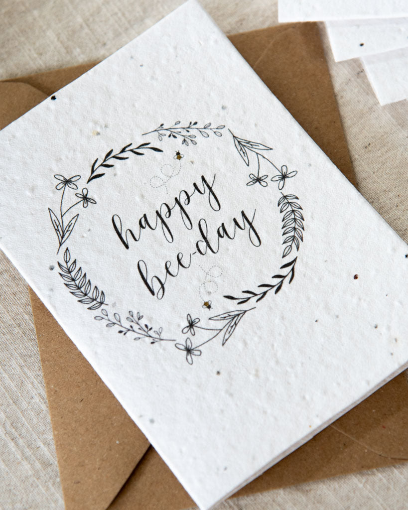 Wildflower plantable seed card with the message 'happy bee-day' and surrounded by botanicals and bees. Sustainable, eco-friendly and can be personalised.
