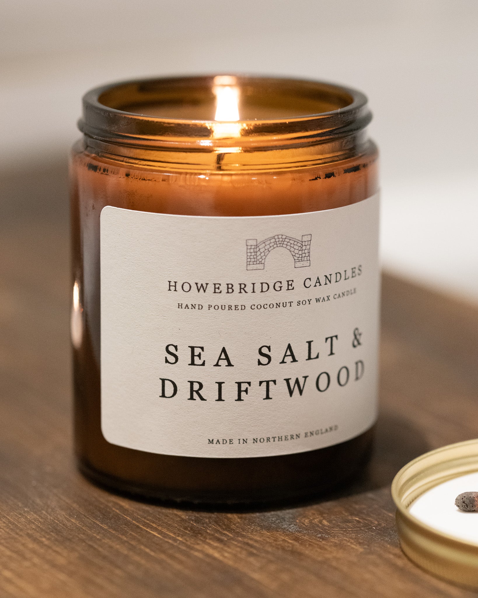 Amber jar candle labeled 'Sea Salt & Driftwood' by Howebridge Candles on a wooden surface.