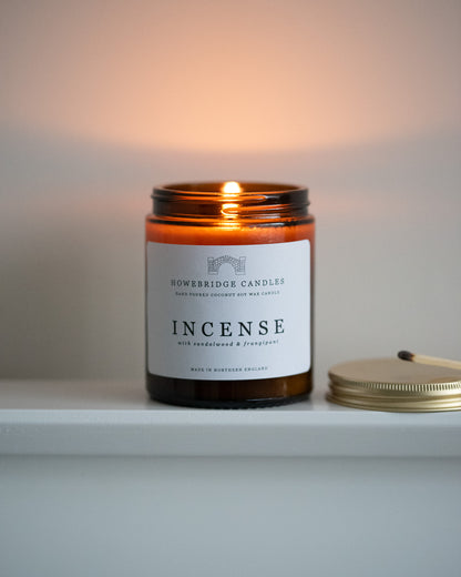 Candle in an amber jar labeled 'Incense' by 'Howeridge Candles' on a white surface with a neutral background.