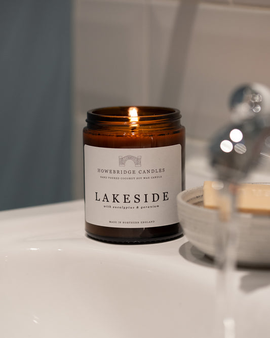 Glass amber candle labeled 'Lakeside' by Howesbridge Candles on a bathroom counter.