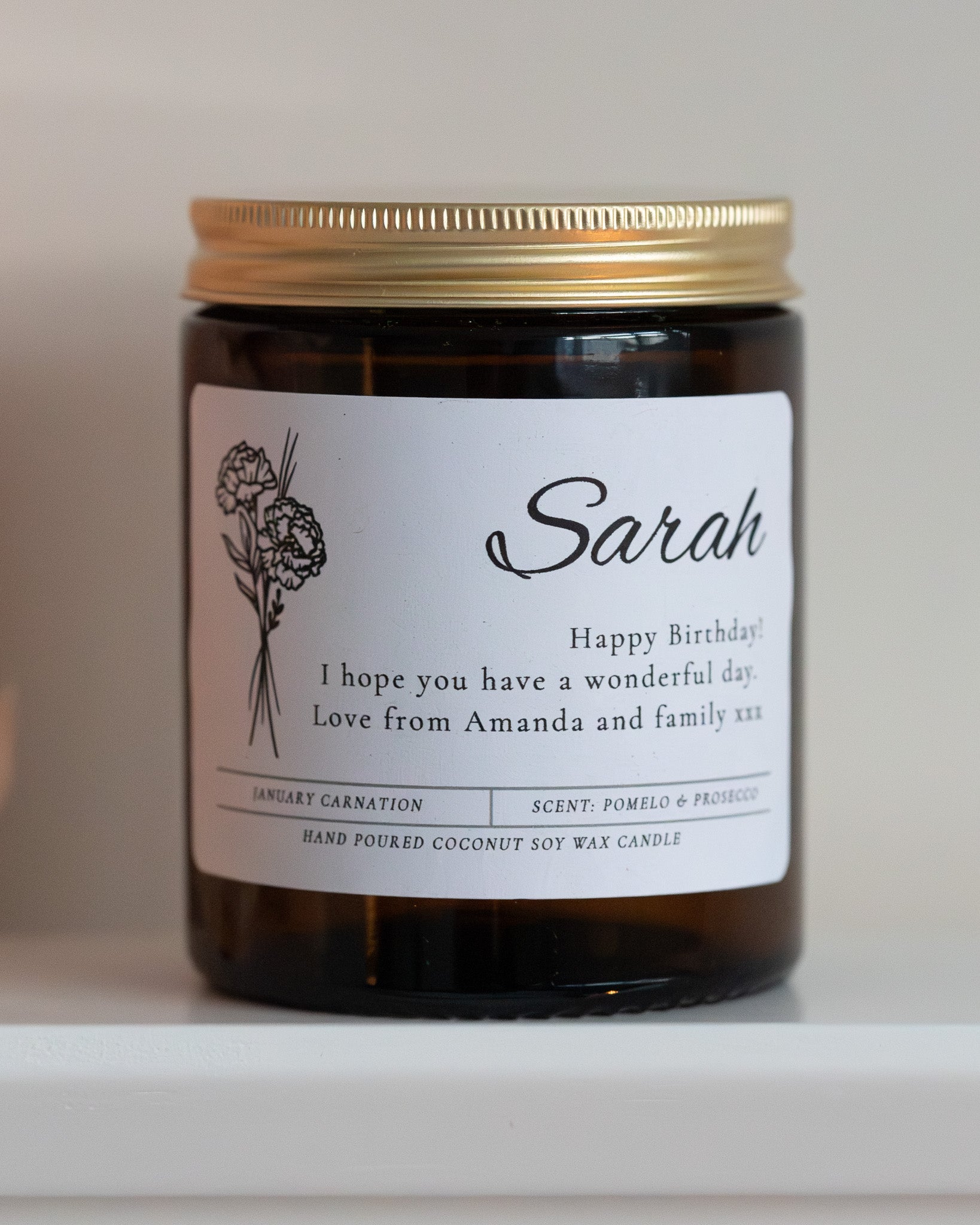Personalised birthday birth flower candle gift by Howebridge Candles, features name, message and birth flower on glass amber jar and gold lid.