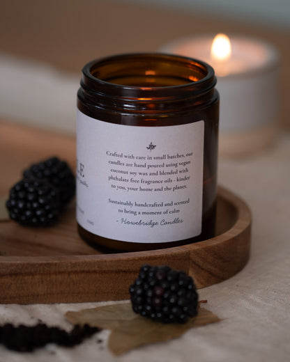 Amber glass candle jar with a off white natural label, close up image of the details on the side, with botanical logo. Talks about ingredients being coconut soy wax and phthalate free oils. How they're sustainable and kinder to you, your home and the planet.