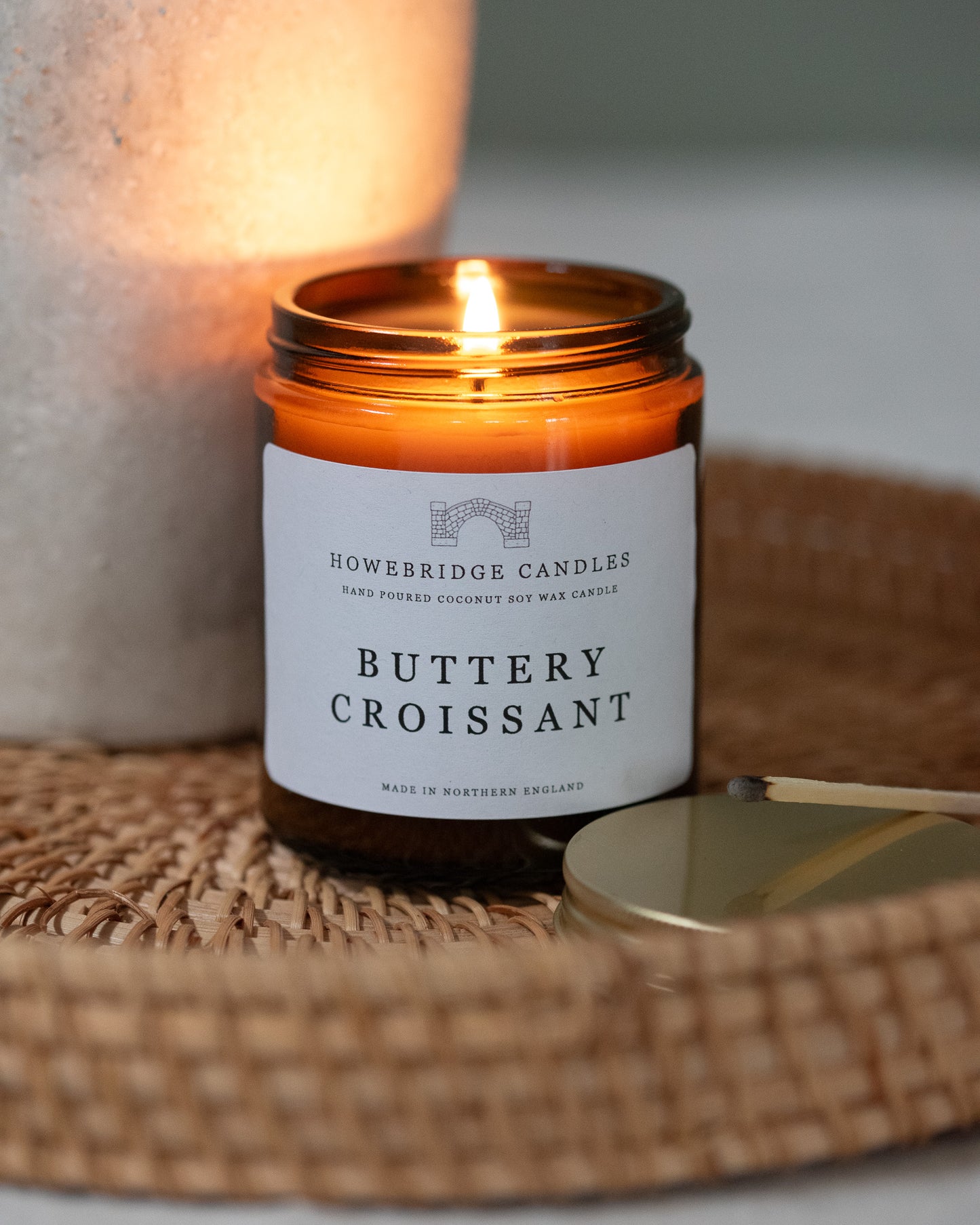 Candle labeled 'Buttery Croissant' by Howbridge Candles on a woven mat.