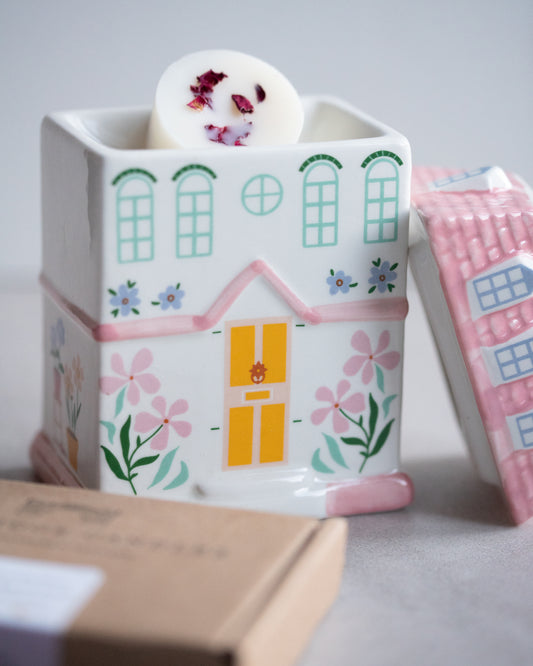 Ceramic pastel house wax burner. The lid has been taken off and a botanical wax melt has been put in the burner.