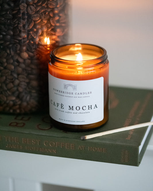 Candle labeled 'Café Mocha' from Howebridge Candles on a book with coffee beans in the background.