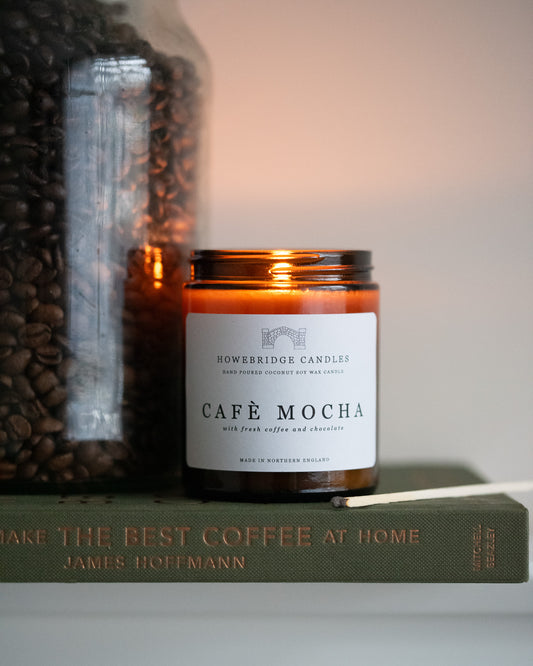 'Café Mocha' candle by Howebridge Canldes, a glass amber candle sat on a green coffee book next to a jar of coffee beans.