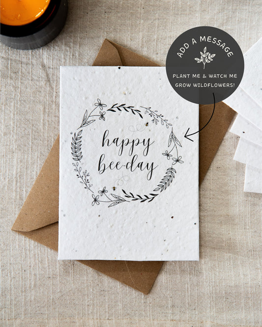 Wildflower plantable seed card with the message 'happy bee-day' surrounded by botanicals, leaves and bees. Printed on 100% cotton paper and complete with c6 kraft envelope. Can be personalised. Sustainable and eco-friendly.