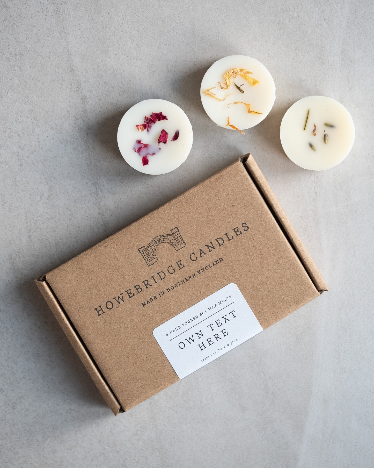 Howebridge Candles personalised soy wax melt letterbox gift. Features label saying "Own Text Here" and surrounded by 3 wax melts sprinkled with dried botanicals. Kraft box is stamped with logo and sealed with personalised label.