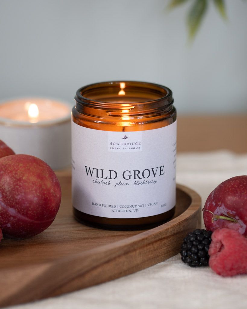 Wild Grove candle lit with fruits on a wooden board. A glass amber jar with a off white wrap around label. Our bestseller rhubarb candle that you will love. A favourite all year round.
