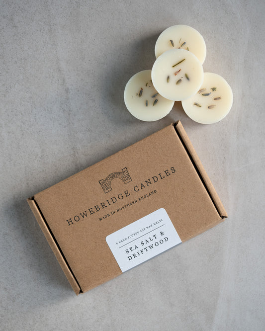 Howebridge Candles sea salt & driftwood soy wax melts, stacked and sprinkled with dried lavender. Next to them is the wax melt packaging, a kraft box stamped with their logo and sealed with a scent descriptive label.
