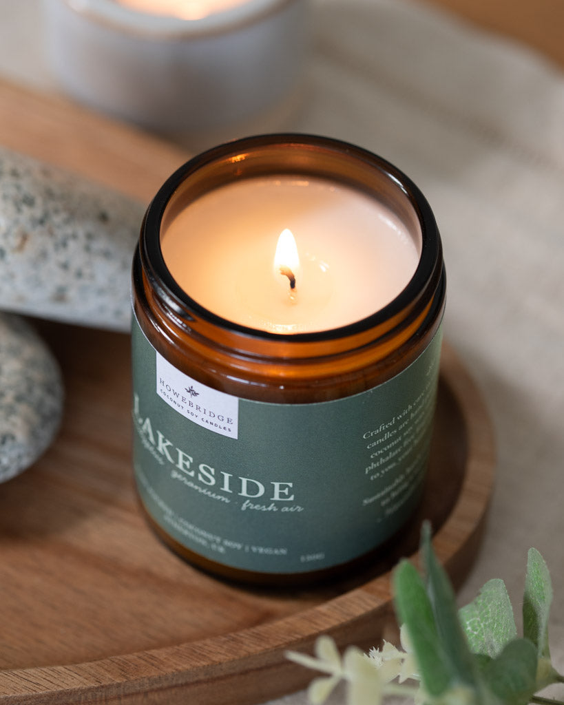 A lit amber jar candle with a sage green label. Scent is Lakeside and smells like the watery breeze whilst sitting next to a lake or waterfall. Hand poured in Howe Bridge.